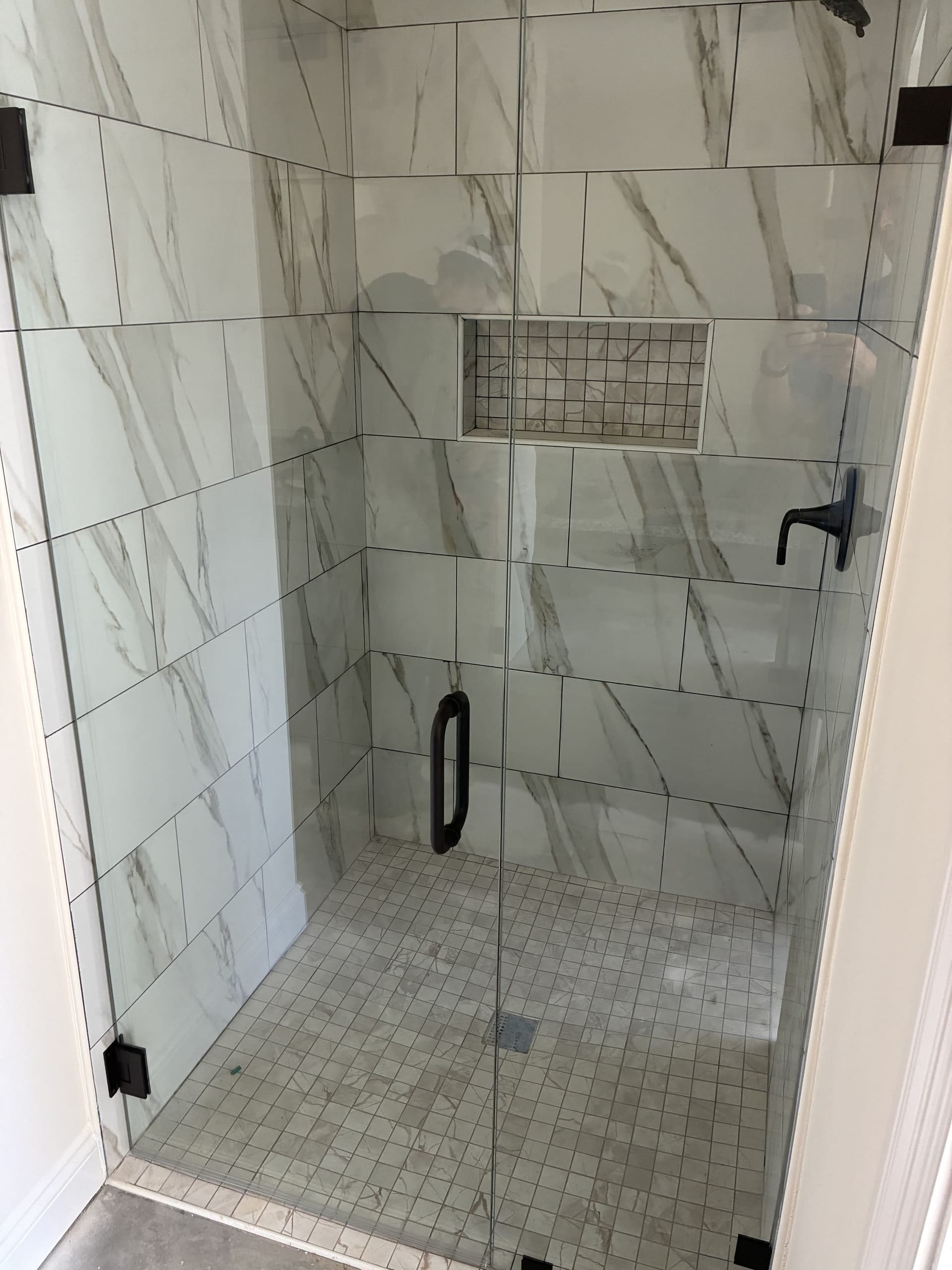 Frameless glass shower enclosure installed in a marble-tiled bathroom