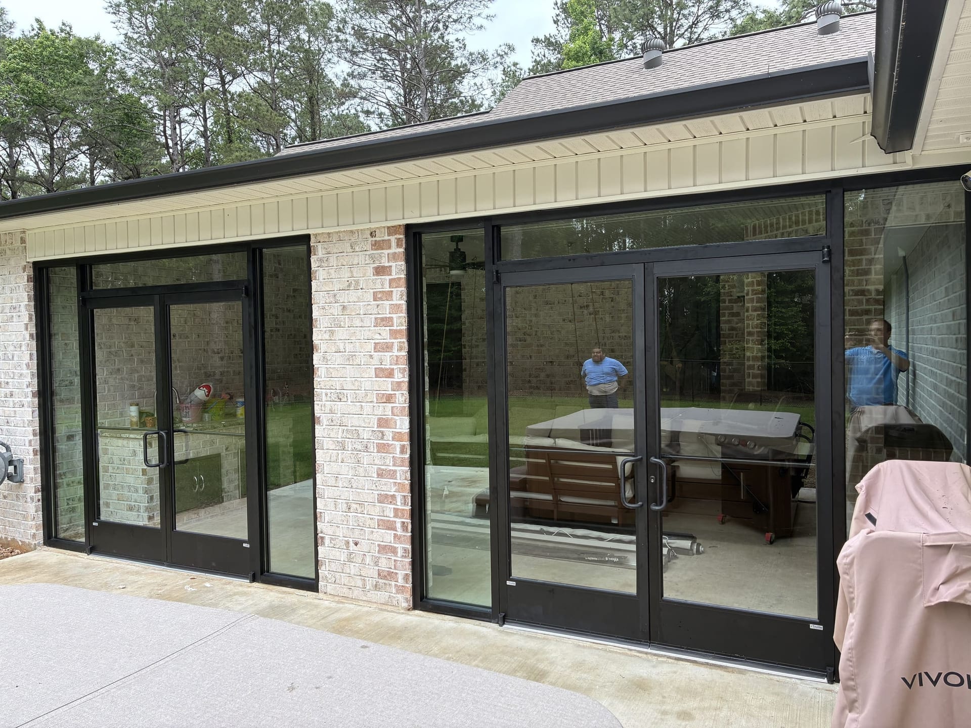 Finished residential sunroom with a wall of black-framed folding glass doors looking out to a brick patio and pine trees